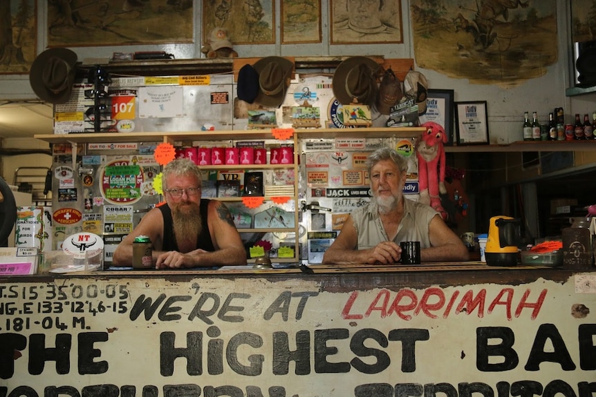 Two men lean on the bar of an outback pub festooned with Australiana.