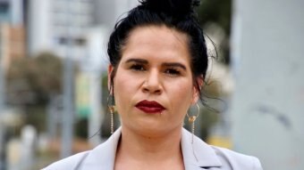 A close up shot of a woman with black hair, a mauve jacket and red lipstick.