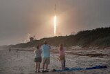 A family on a beach watches a rocket launch.