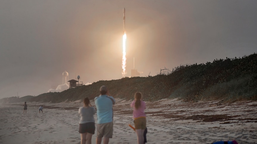 A family on a beach watches a rocket launch.