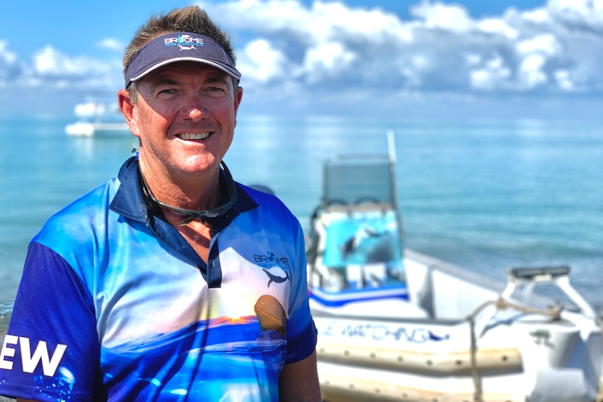 A man on a beach with a boat in the background.