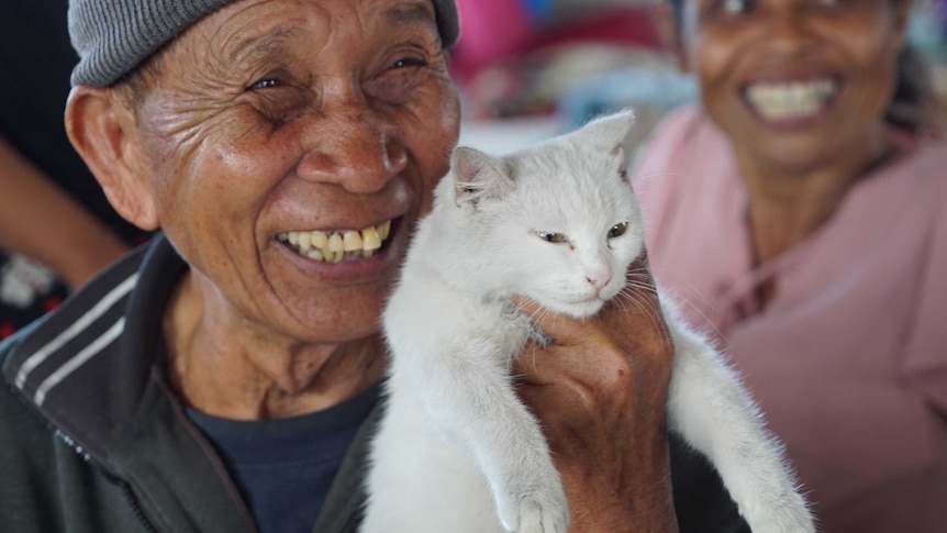 I Kembar smiles and holds up his white cat.