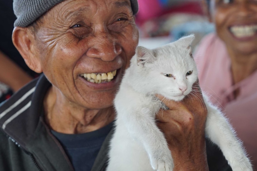 I Kembar smiles and holds up his white cat.