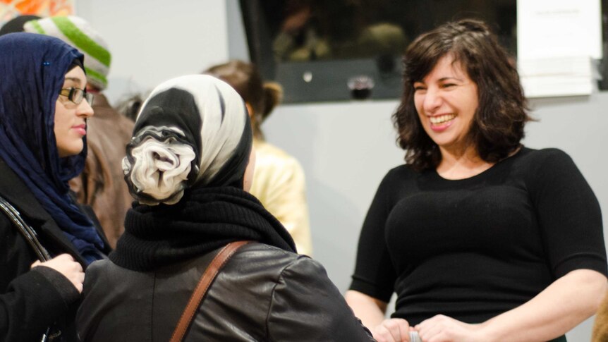 A woman with dark hair speaks to two women wearing headscarves at an event opening.