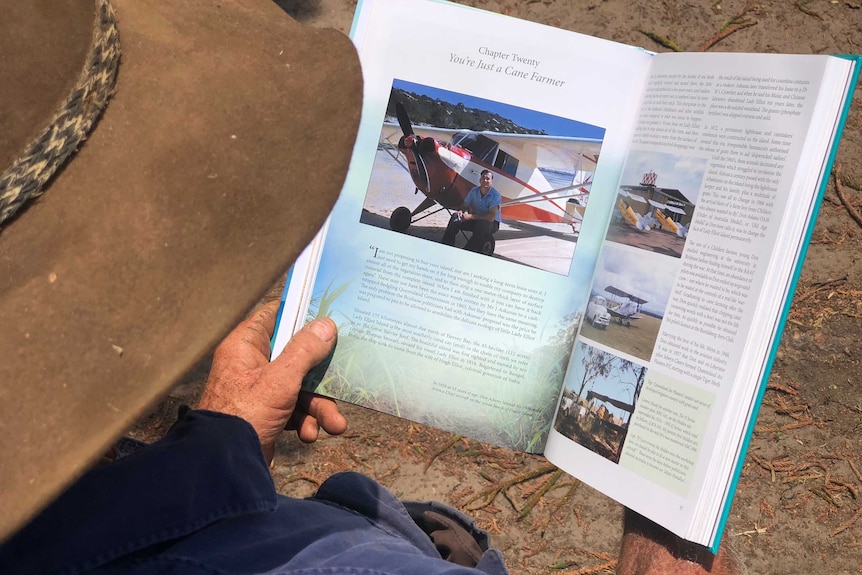 Man holding open book looking at page with don adams standing by a red plane.