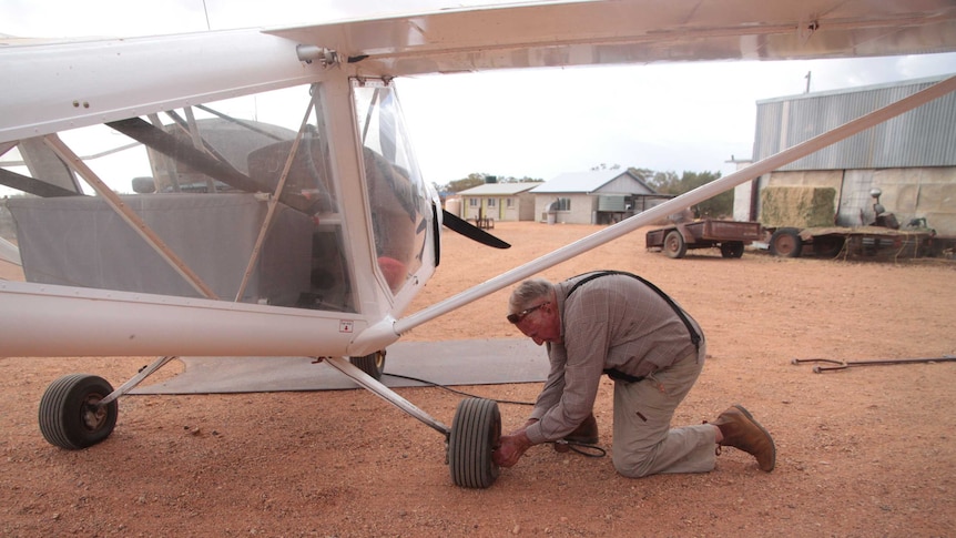 Doug kneeling down on the red dirt, pushing the needle of the pump into the flat tyre on the plane.