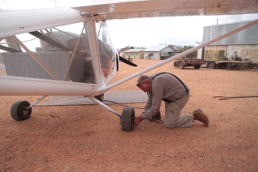 Doug kneeling down on the red dirt, pushing the needle of the pump into the flat tyre on the plane.