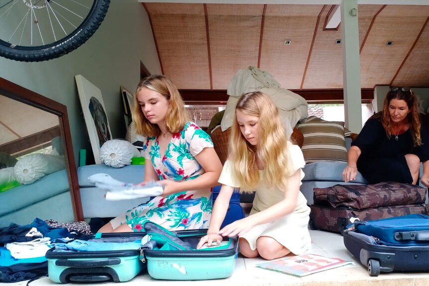 Two girls with blonde hair pack up suitcases in a bedroom 