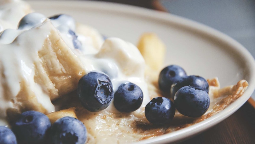 Blueberries and banana on pancake in white plate on wooden table.