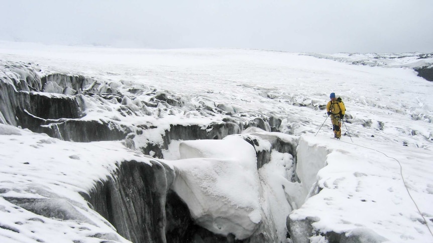 A man in a yellow snowsuit on a glacier