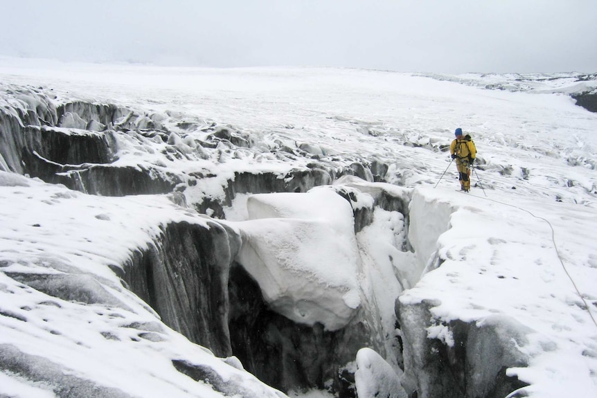 A man in a yellow snowsuit on a glacier