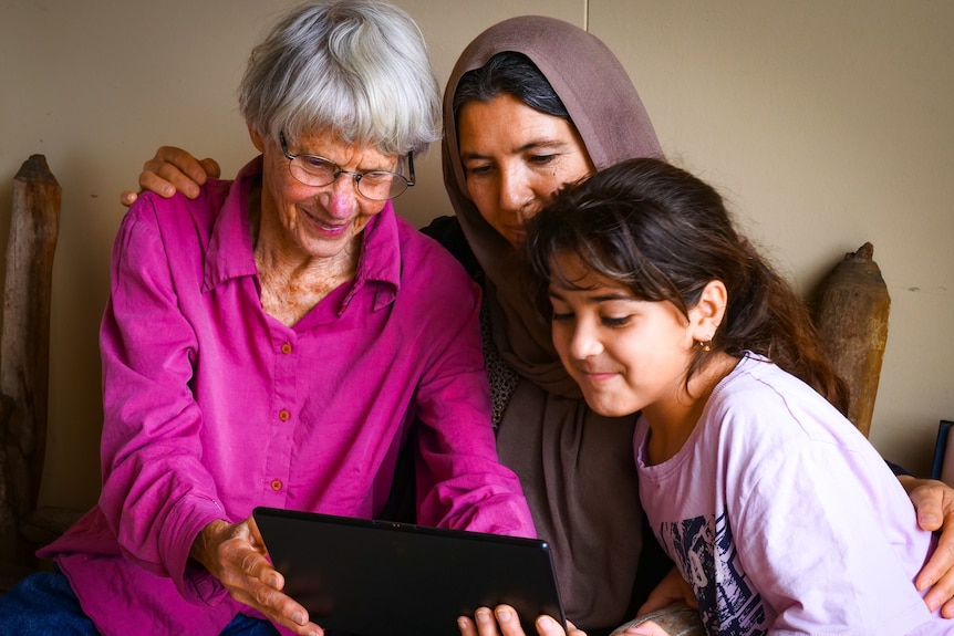 Two women and a girl look at an ipad