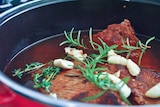 Brisket stew in a red pot garnished with rosemary, thyme and butter for a story about how to cook brisket.