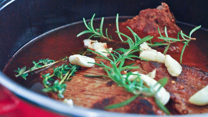 Brisket stew in a red pot garnished with rosemary, thyme and butter for a story about how to cook brisket.