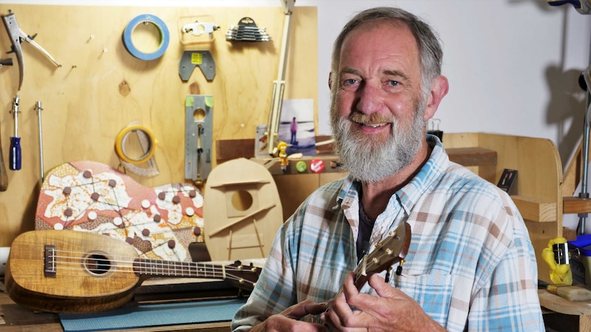 A man playing a ukulele he made in his workshop