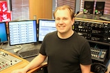 Andrew Davies — distribution and engagement coordinator for ABC Audio Studios  smiles at the camera in a radio sound booth.