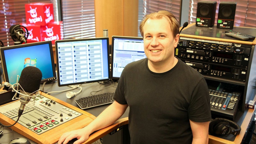 Andrew Davies — distribution and engagement coordinator for ABC Audio Studios  smiles at the camera in a radio sound booth.