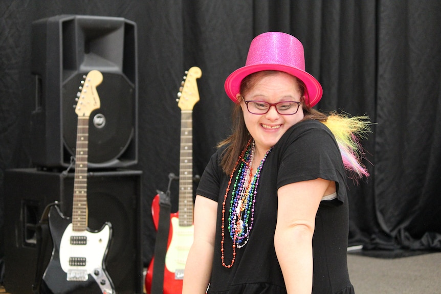 A woman with a pink hat in front of two guitars. 