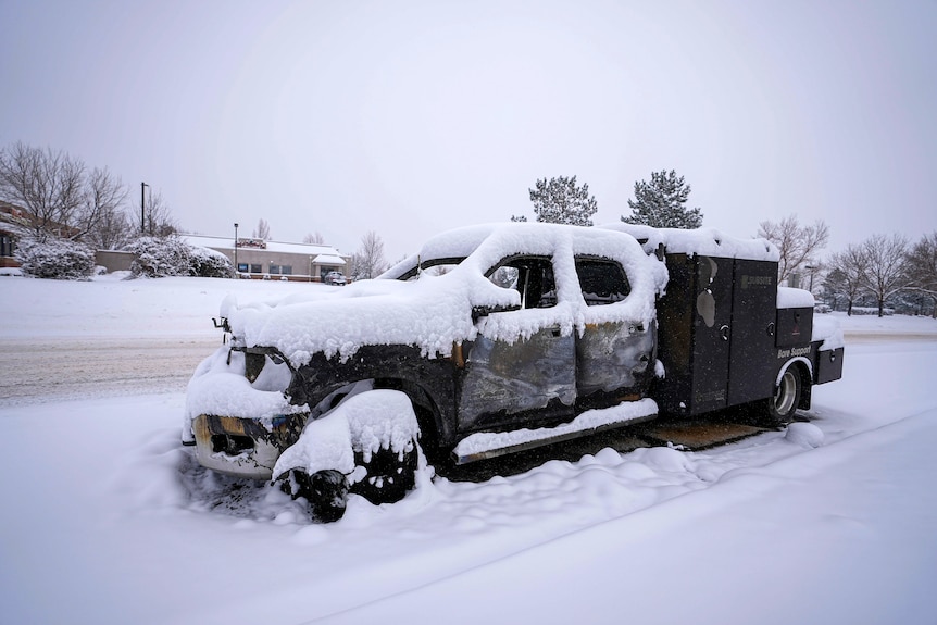 Snow covers the burned remains of a truck left on the road.