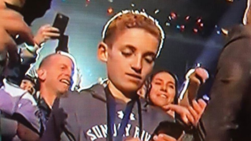 A kid looks at his phone in the middle of a cheering crowd at the Super Bowl.