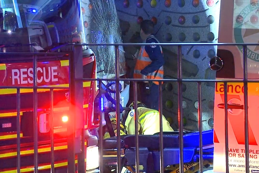 bus with broken windshield against wall with emergency services around