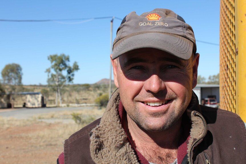 Close portrait photo of Ben Heaslip standing outside on the station. He has faded cap on and bushland and a mountain are behind.