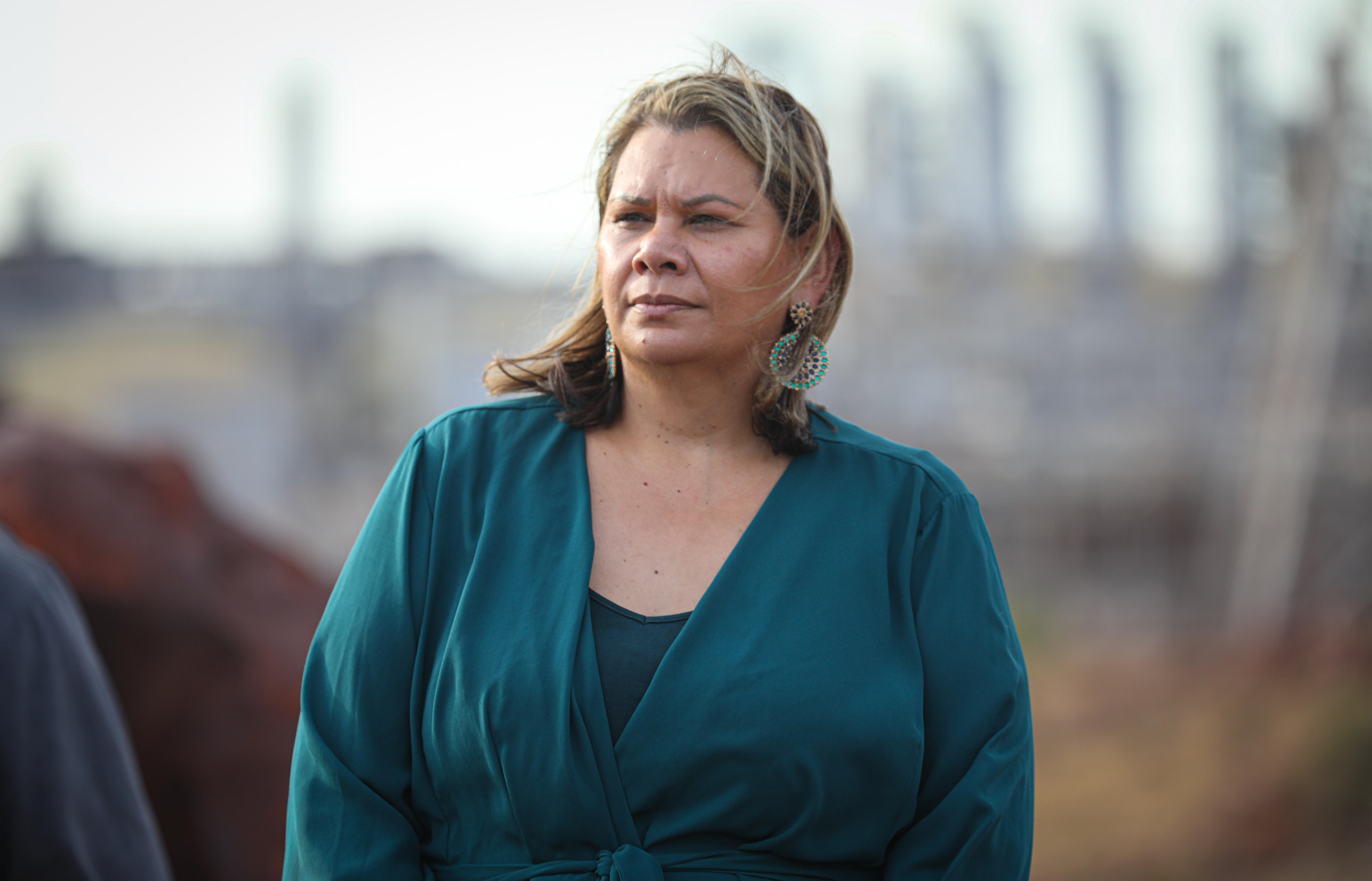 A woman wearing a dark green dress looks off to the side, frowning.