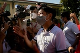 Ferdinand Bongbong Marcos Jr, wearing a face mask, gestures as he walks through a crowd of cameras.