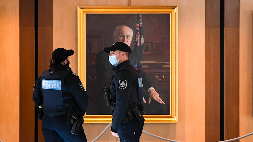 Two police officers wearing masks in front of a mural of John Howard.