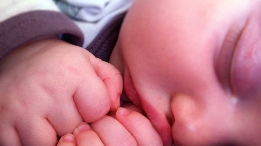 A sleeping baby bunches its hands up under its chin.