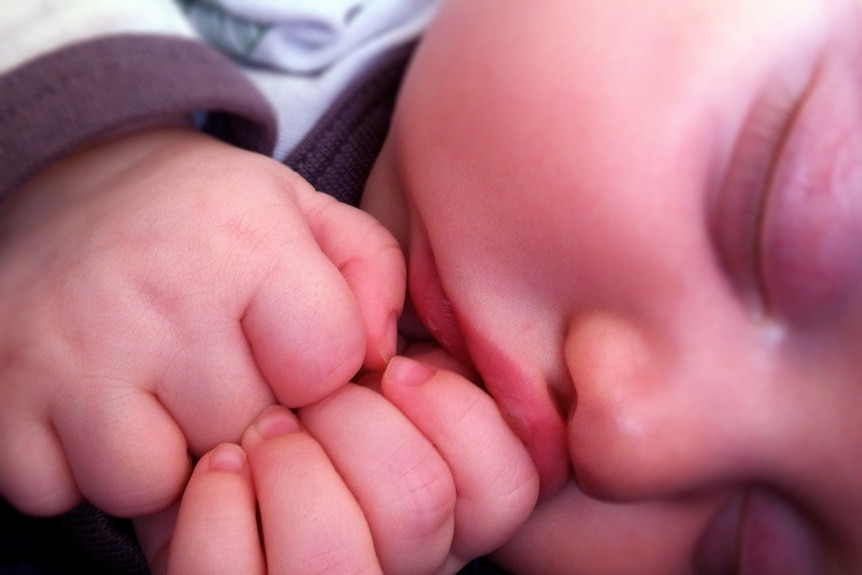 A sleeping baby bunches its hands up under its chin.