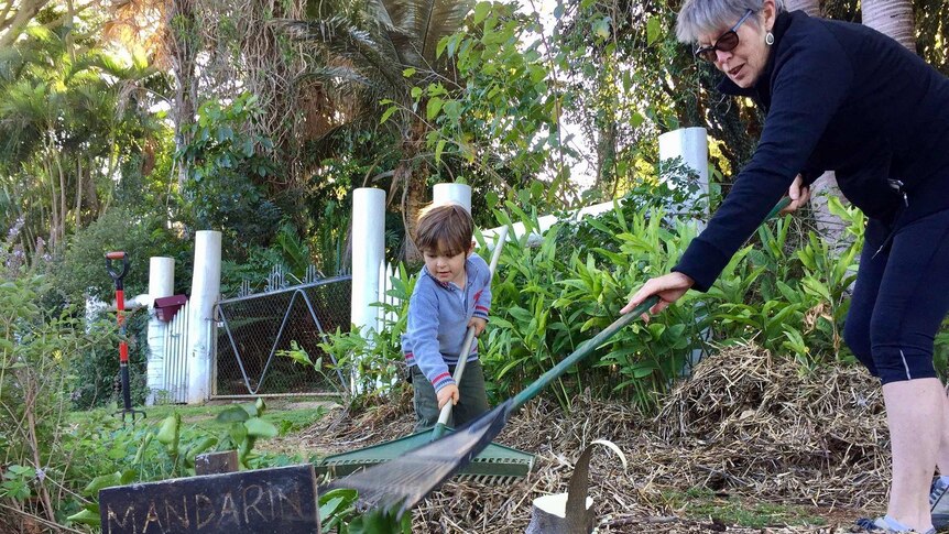 Young boy and an older woman rake mulch together on the footpath.