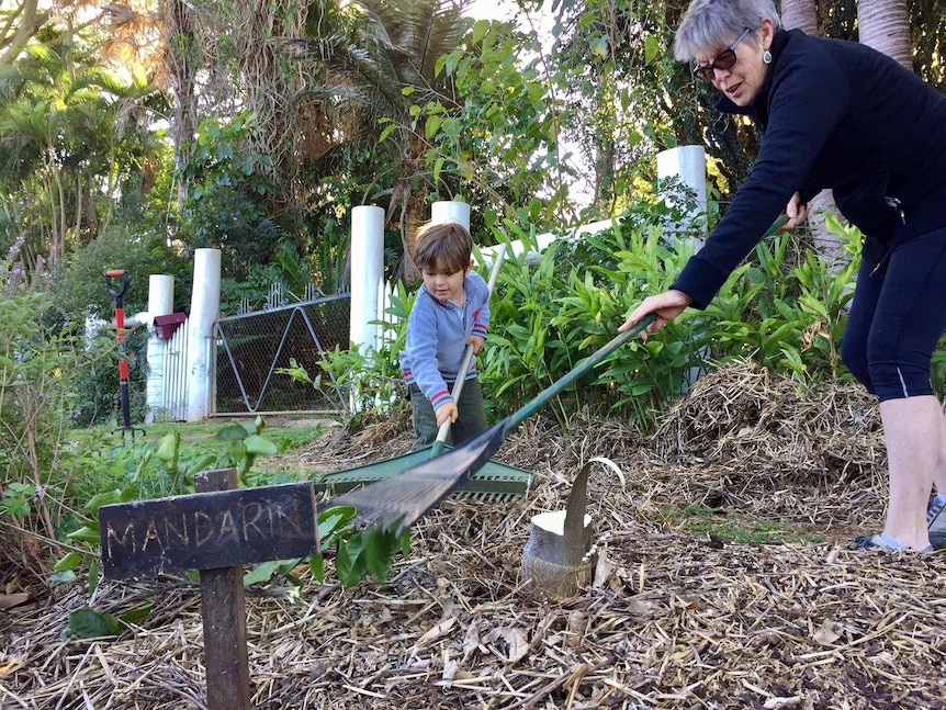 Young boy and an older woman rake mulch together on the footpath.