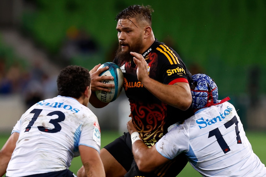 A chiefes player holds the ball as he is tackled by Waratahs opponents.