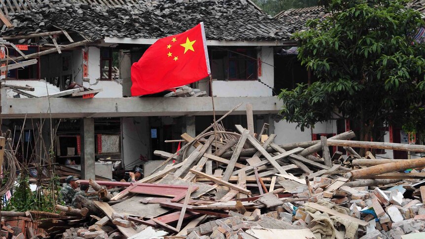 A Chinese national flag flies in the ruins of houses.