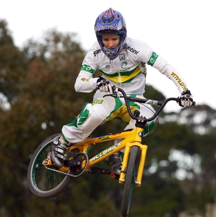 A young woman jumping on a BMX bike wearing a helmet and uniform