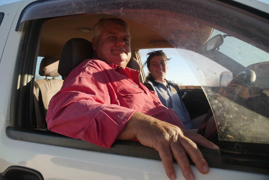 A man and a young girl look at the camera from a car window.