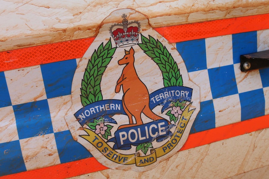 The NT Police emblem on a police vehicle covered in red dirt.