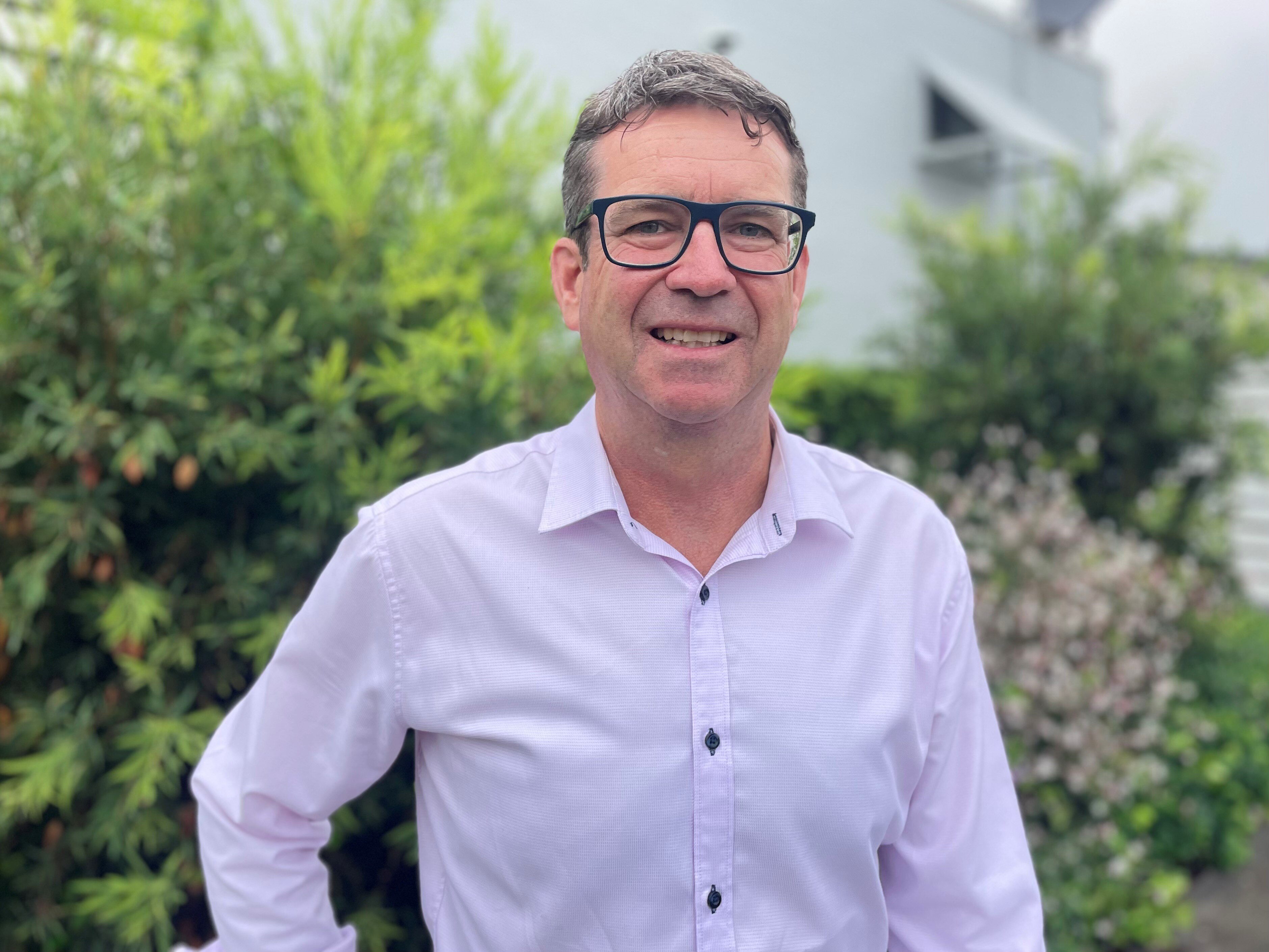 Robery Dwyer smiling with glasses on and a pink shirt 