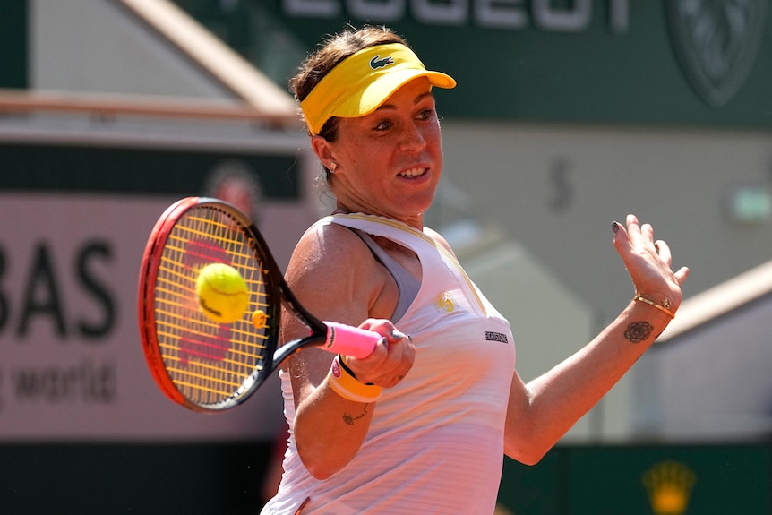 A tennis player holds her racquet out horizontally as she connects with the ball for a forehand return.. 