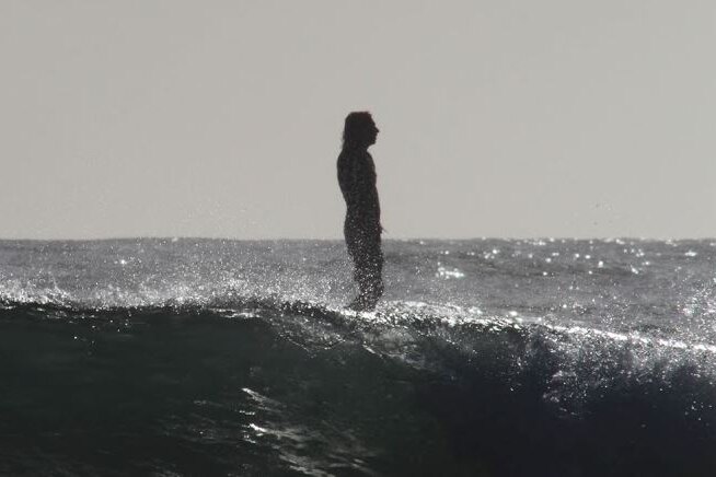 A man in silhouette standing on a surfboard in the ocean.
