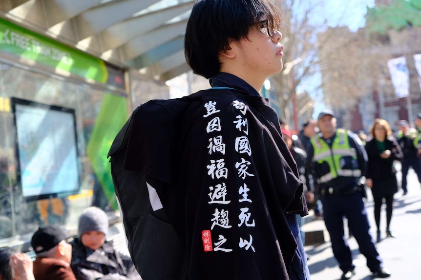 A man stands in front of a tram stop with a t-shirt with Chinese characters.