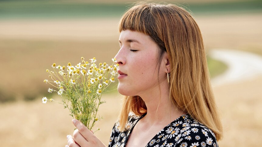 Woman with eyes closed smelling a bunch of chamomile