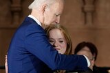 Joe Biden, wearing a blue suit, hugs a young woman.