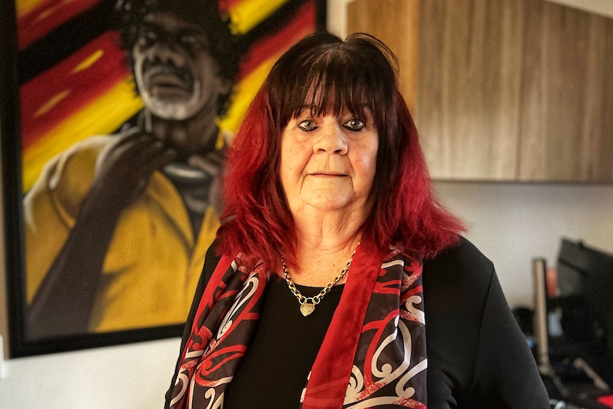 A woman in front of a painting of an Aboriginal man. 