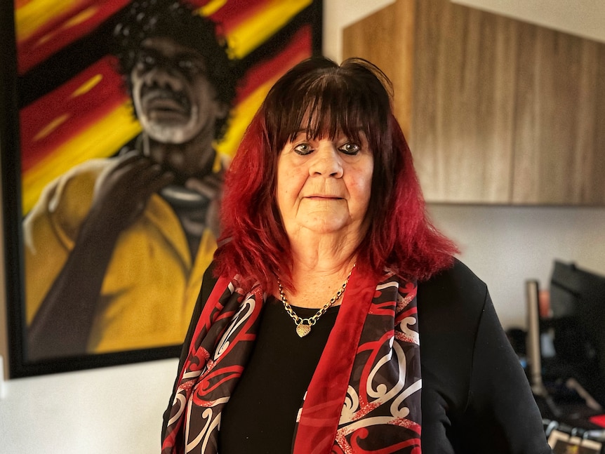 A woman in front of a painting of an Aboriginal man. 