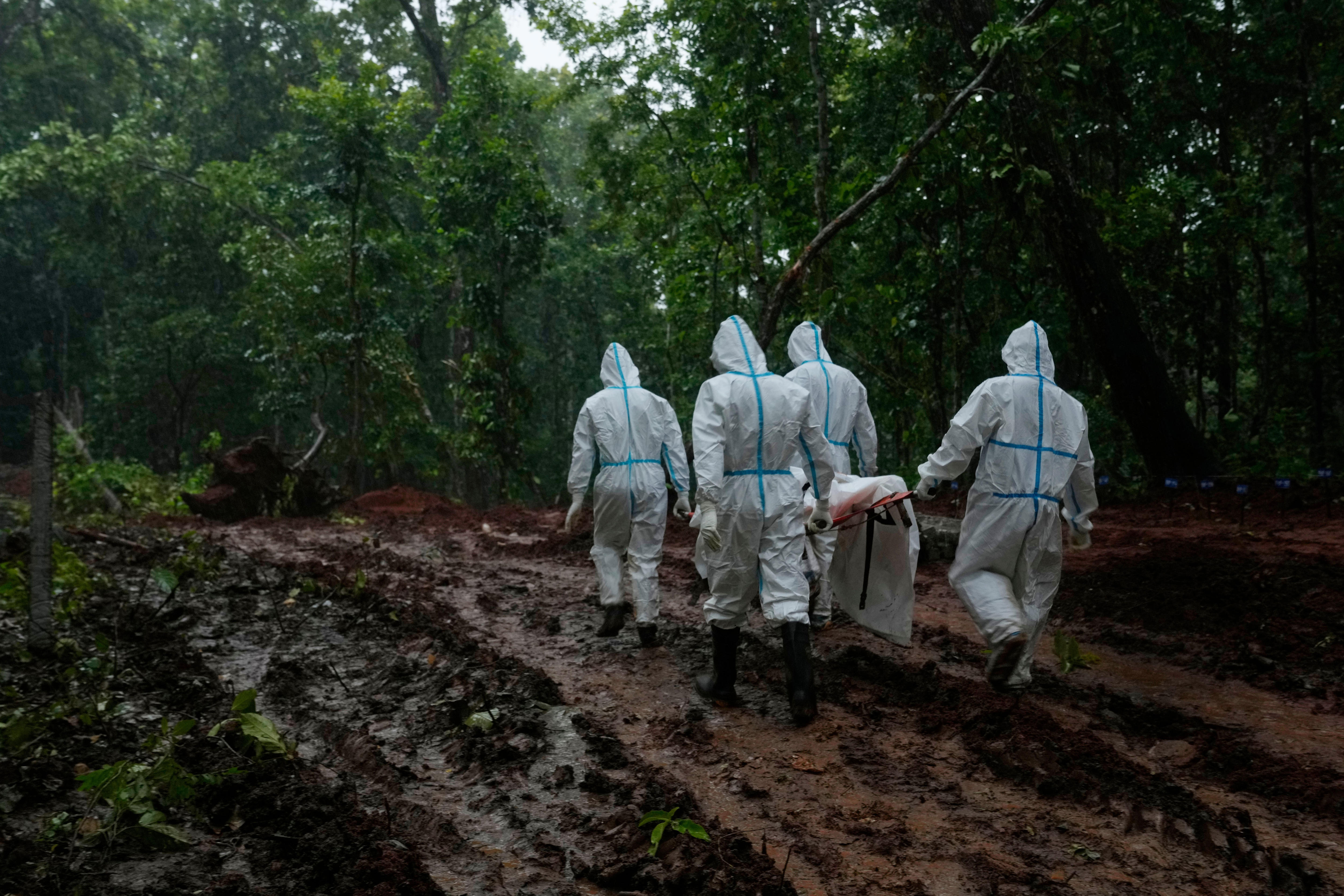 Four people in white hazmat suits carry a body under a white sheet on a stretcher