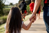 A girl holding hands with an adult.