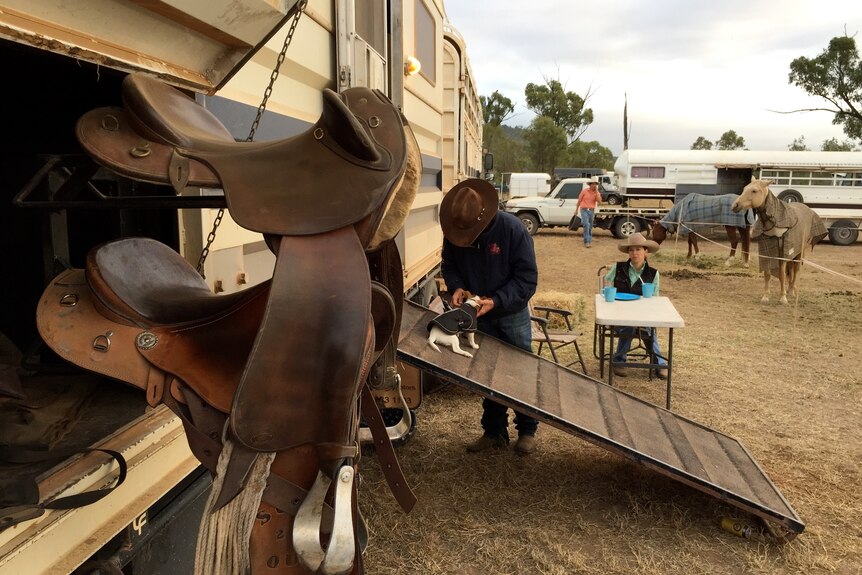 Mac Shann plays with a small dog beside a large horse trailer.