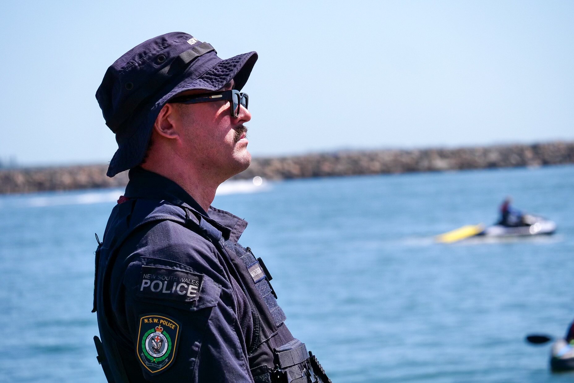 NSW Police officer wearing hat and sunglasses looking out at Newcastle Harbour. 